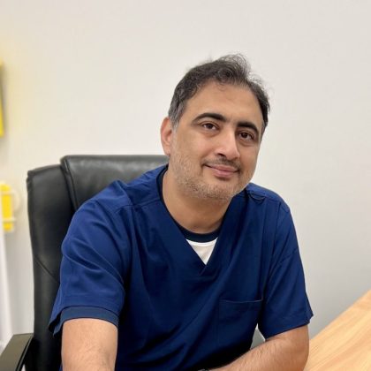 Dr Imran Hilal smiles at the camera. He is wearing navy scrubs